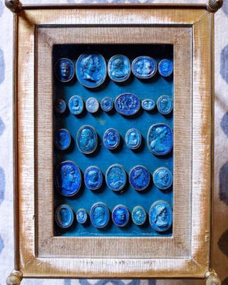 Antique European Grand Tour intaglio collection featuring classical portrait medallions in deep blue with aged gilt frames displayed in a shadow box used as inspiration for the Capri Intaglio Patina Finish by Amy Howard At Home