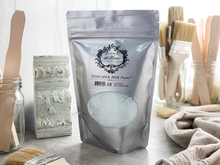 A package of Toscana Milk Paint in Cote D' Azure color, with a background featuring brushes and a painted piece of furniture.