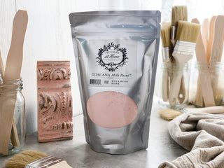 A silver pouch of Toscana Milk Paint powder in Toulouse Rose color, displayed alongside brushes and a decorative item.