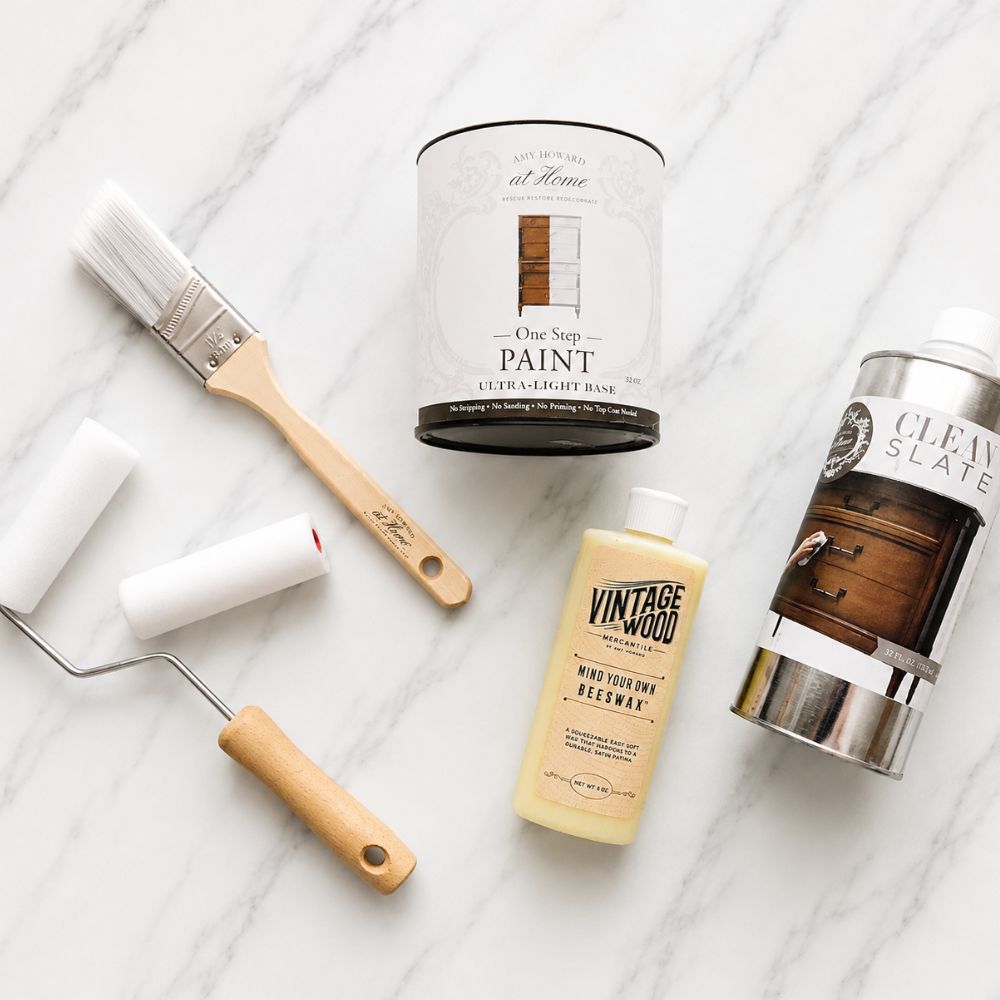 Amy Howard At Home One Step Paint beginner bundle, brush, foam roller, beeswax, and Clean Slate surface prep on marble background