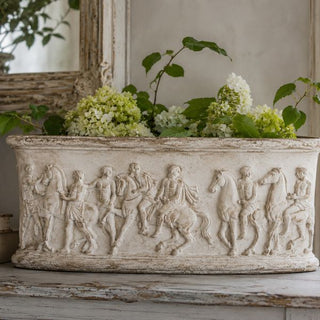 Classical Greek frieze detail from the Amy Howard At Home Relief Decorative Mould applied to a decorative planter filled with white hydrangeas styled on an antique painted surface