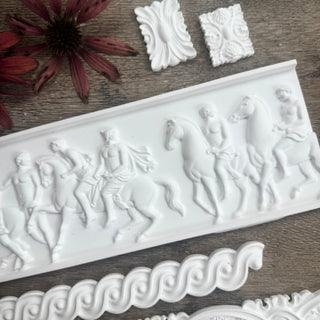 Close up flat lay of CeramiCast castings from the Amy Howard At Home Relief and Rolling Coin Decorative Moulds showing classical frieze panel and ornamental trim details on a grey wood surface with dried pink echinacea