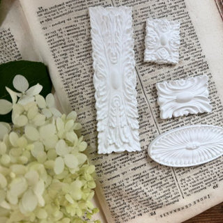 CeramiCast castings from the Amy Howard At Home Rolling Coin Decorative Mould showing ornamental appliqué details on an antique book with white hydrangeas