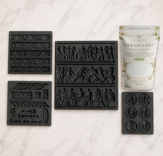 A set of black ceramic casting molds and a tube of Ceramicast clay modeling compound arranged on a white marble surface. The molds include various decorative and figurative relief patterns, and the tube is labeled Ceramicast.