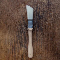 A square specialty brush with white bristles and a wooden handle, placed on a wooden surface.